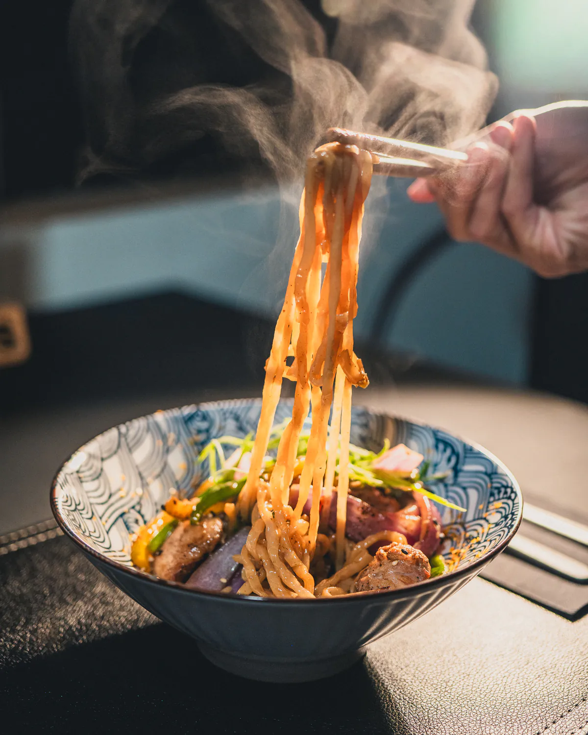 Fideos salteados levantados con palillos sobre un bowl humeante