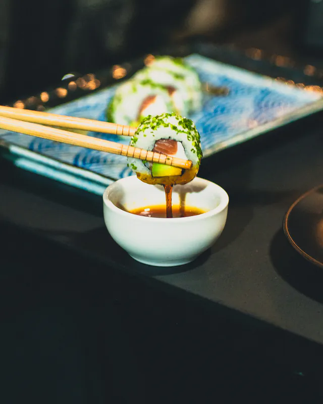 Pieza de sushi con palta y salmón mojada en salsa de soya